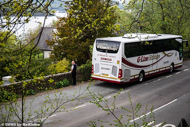 A coach driver stands beside his bus in a lay-by on the edge of Ambleside as visitors make the most of their day