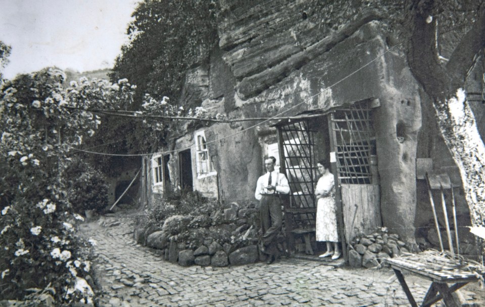 Black and white photo of a man and woman standing outside a rock house.
