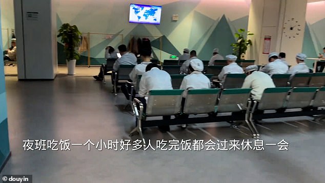 Staff in uniforms are seen sat looking at their phones during a work break at a Chongqing factory