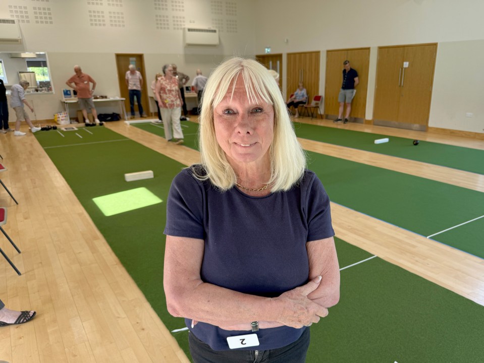 Woman standing in a hall with indoor bowling greens in the background.