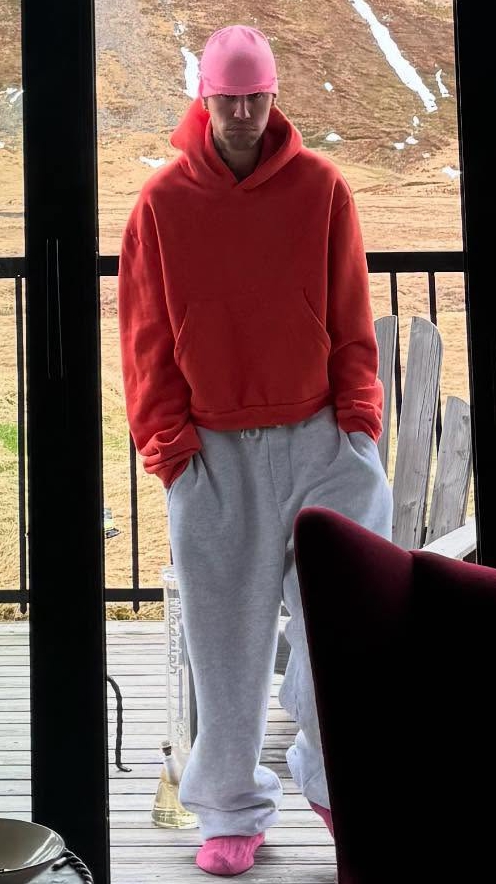 Justin Bieber and two others on a balcony overlooking a mountain landscape.  One person appears to be smoking.