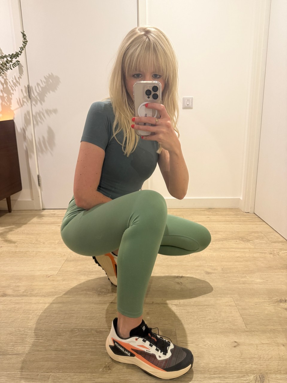 Woman in sage green leggings and Salomon trail running shoes taking a selfie.