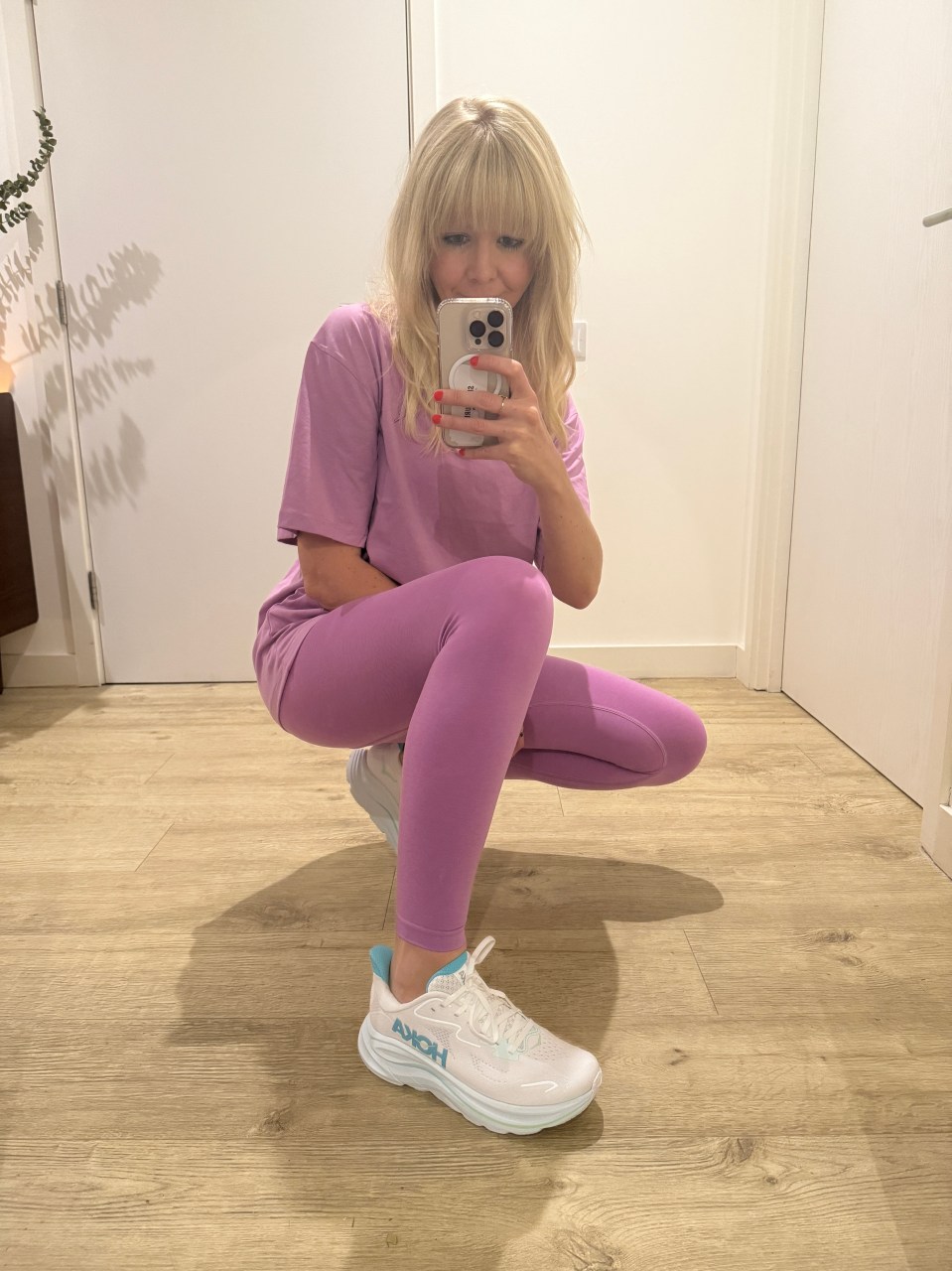 Woman in purple leggings and shirt taking a selfie while showing off her new Hoka running shoes.