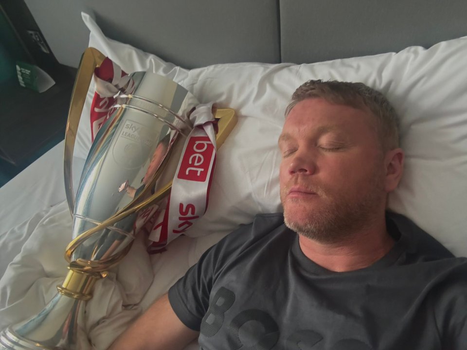 Man sleeping in bed next to a trophy.