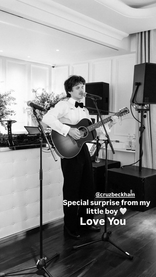 Black and white photo of Cruz Beckham singing and playing an acoustic guitar.