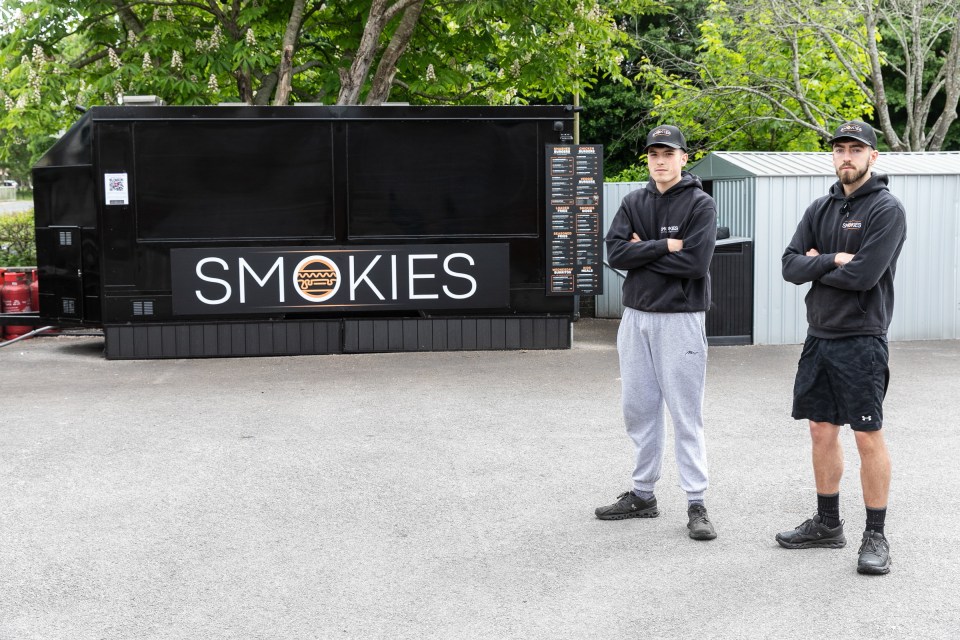 Two men stand in front of their closed smash burger van, Smokies.