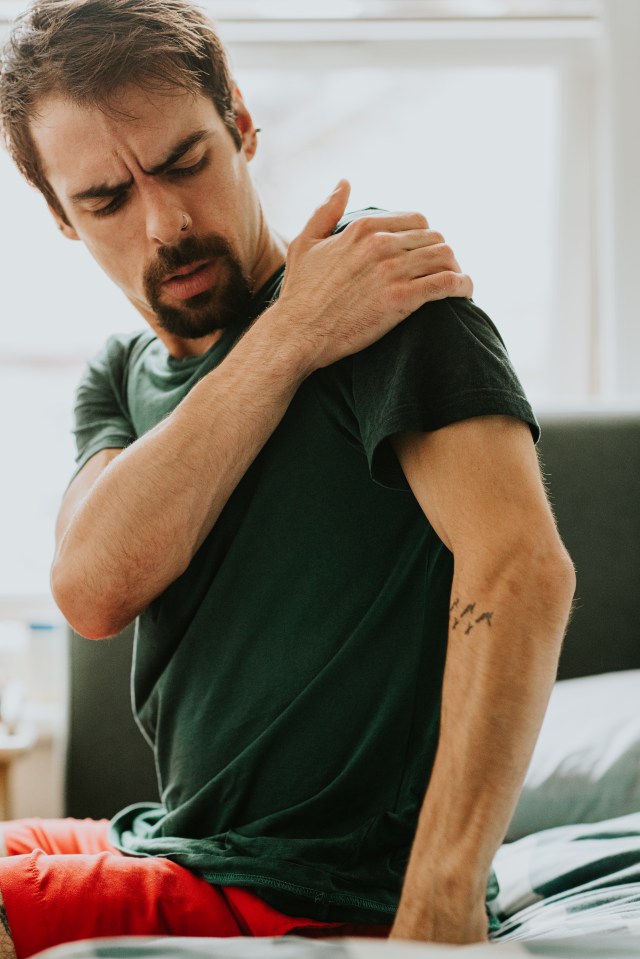 Man grimacing in pain while rubbing his shoulder.