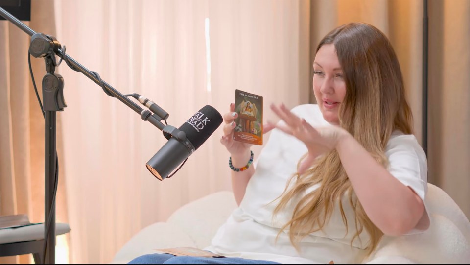 Woman holding a tarot card during a podcast interview.