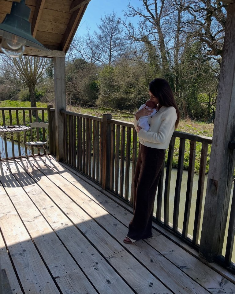 Woman holding a baby on a deck overlooking a waterway.
