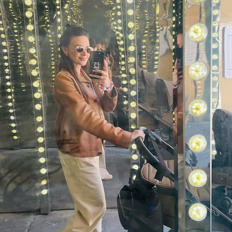 Woman in brown jacket taking a selfie in a mirrored room with lights.