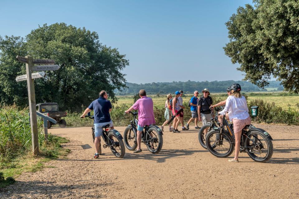 Holidaymakers on e-bikes at a North Norfolk coast signpost.