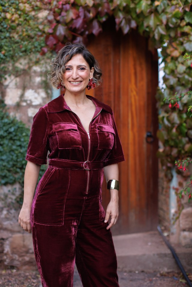 Woman in a burgundy velvet jumpsuit smiling.