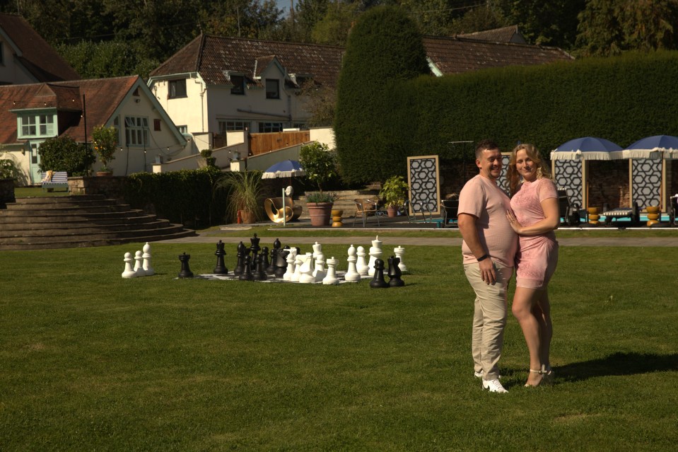 Couple standing on a lawn with a giant chessboard in the background.