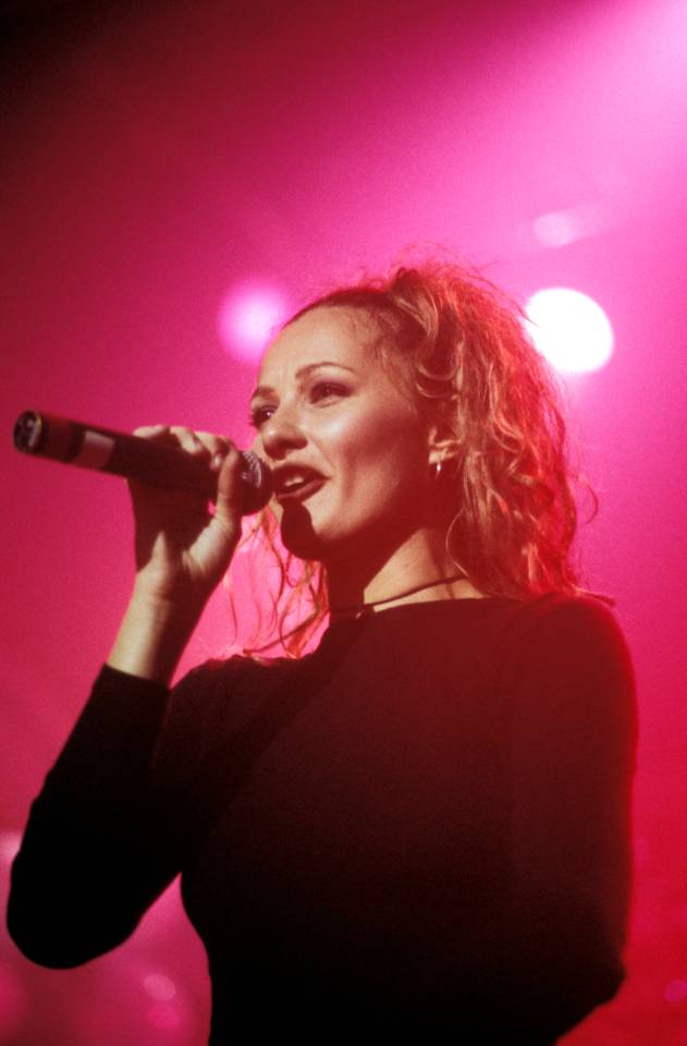 a woman singing into a microphone with a pink background