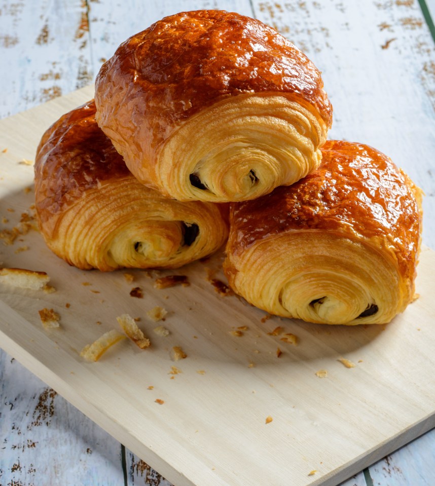 Three chocolate croissants on a wooden board.