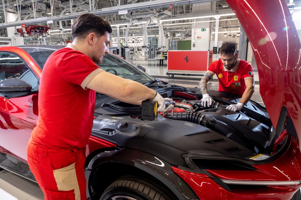 Two workers in red Ferrari shirts working on a red Ferrari's engine.
