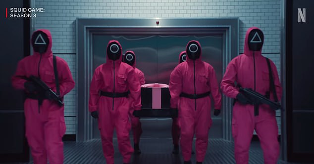 The trailer begins with the mysterious pink-clad men carrying in a coffin to the players' dormitory area, as it's revealed a very alive Gi-hun is in the box