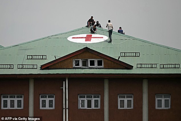 Workers paint a red cross symbol over the roof of a hospital as a preventive measure amid the ongoing border tensions, in Srinagar on May 7, 2025