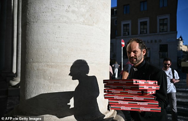 A man walks holding pizza boxes, casting a shadow on a pillar of the colonnade, a day prior to the start of the conclave, near The Vatican, in Rome, on May 6, 2025