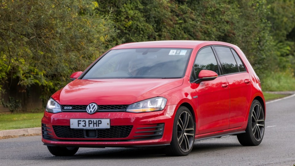 Red Volkswagen Golf driving on a road.