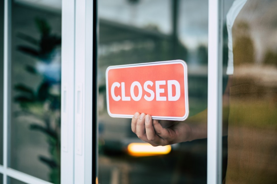 Person placing a "Closed" sign on a coffee shop door.