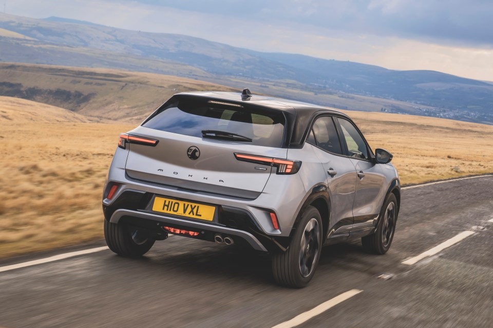 Rear view of a silver Vauxhall Mokka Hybrid driving on a road.
