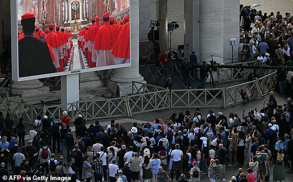 Visitors watch the cardinal's procession to the Sistine Chapel displayed on a screen, ahead of the conclave, on St Peter's Square in the Vatican, on May 7, 2025. (Photo by Filippo MONTEFORTE / AFP) (Photo by FILIPPO MONTEFORTE/AFP via Getty Images)