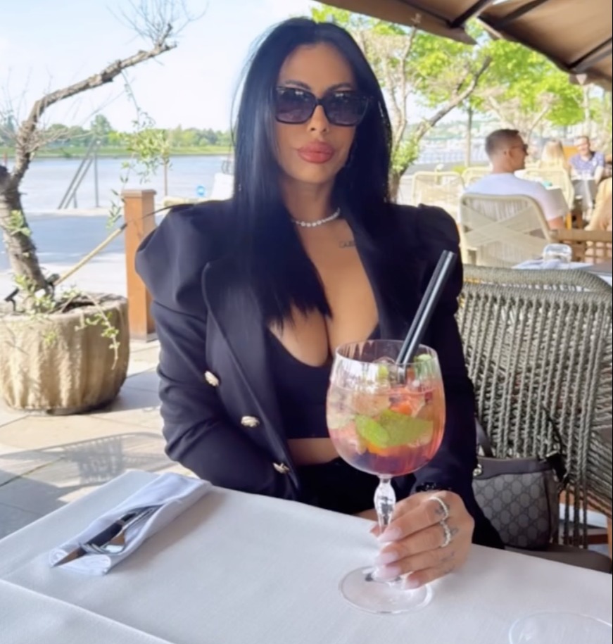 Woman sitting outdoors at a restaurant table, drinking a cocktail.