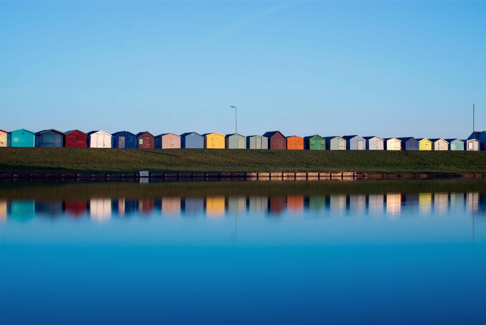 Colorful beach huts reflected in a calm lake.