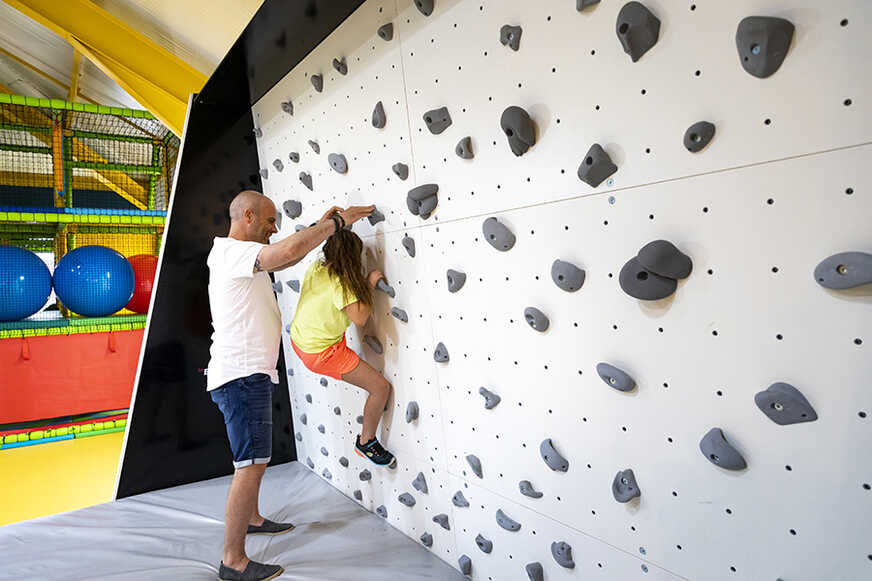 A man helps a girl climb a climbing wall.