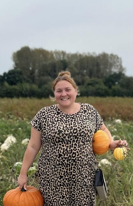 Woman in leopard print dress holding pumpkins in a field.