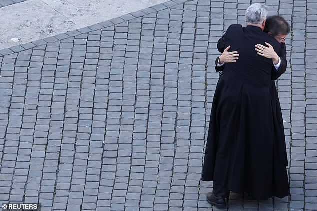 Priests embrace each other as they react to white smoke from the chimney on the Sistine Chapel