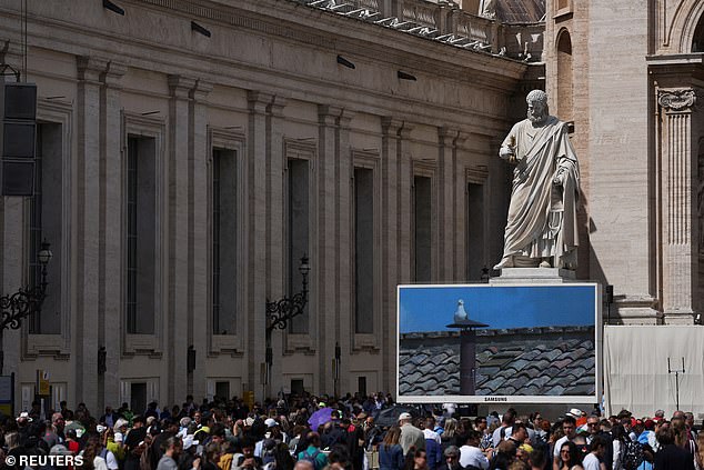 People gathered near a screen displaying a live feed of the chimney on the Sistine Chapel