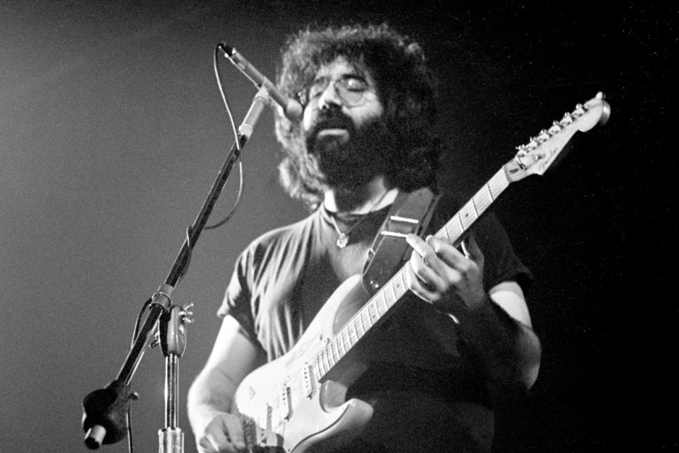 Black and white photo of Jerry Garcia playing guitar.