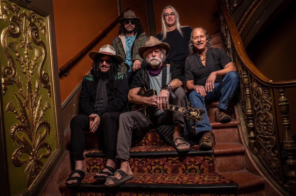 Five men sitting on a staircase, one holding a guitar.