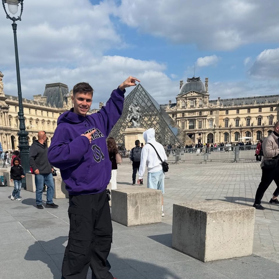 Romeo Beckham in Paris, gesturing towards the Louvre Pyramid.