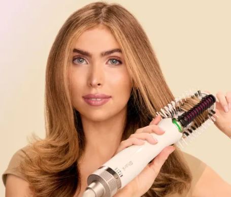 Woman using a hot styling brush on her long hair.
