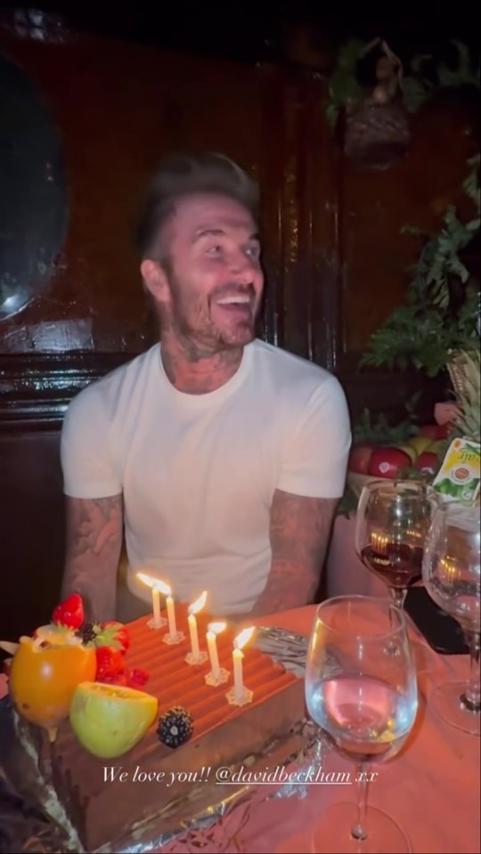 David Beckham smiling at a birthday cake with lit candles.