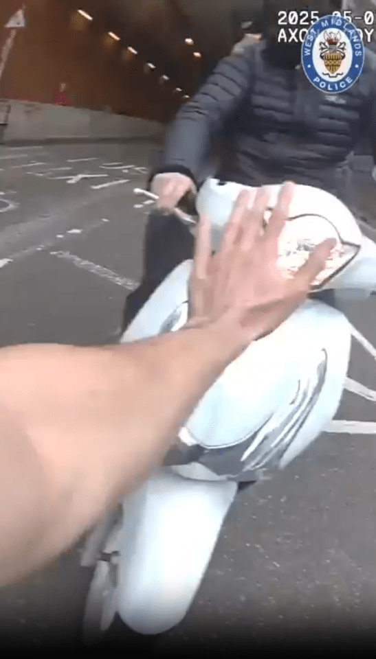 Screenshot of a hand stopping a white scooter in a tunnel.