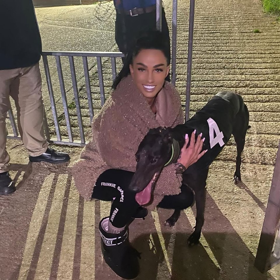 Woman crouching and hugging a racing greyhound wearing a racing bib with the number 4.