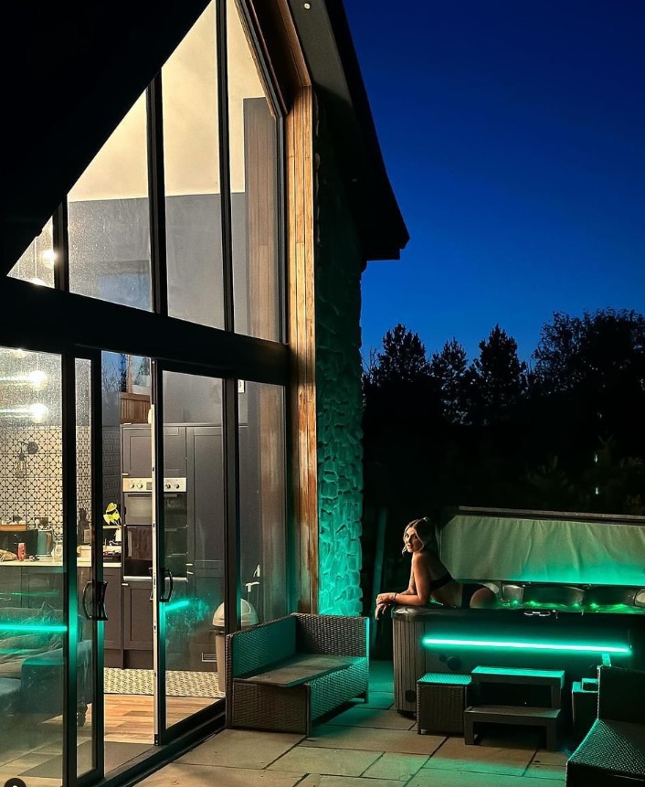 Woman relaxing in a hot tub outside a luxury barn at night.