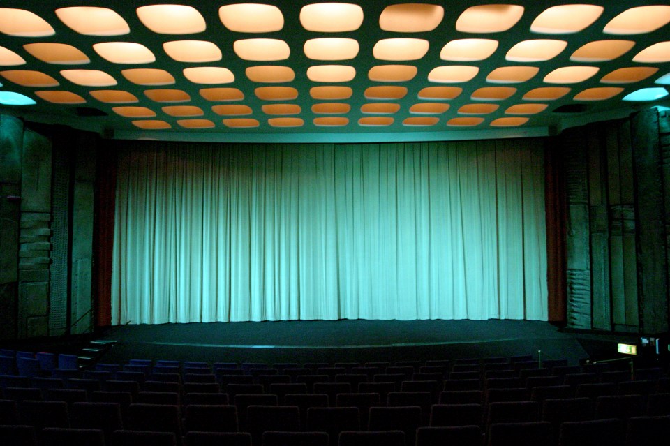 Empty movie theater auditorium with teal curtains and a patterned ceiling.