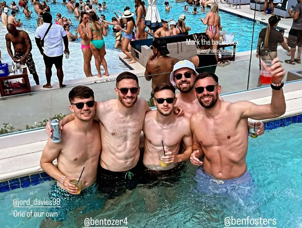 Four shirtless men in a pool with drinks.