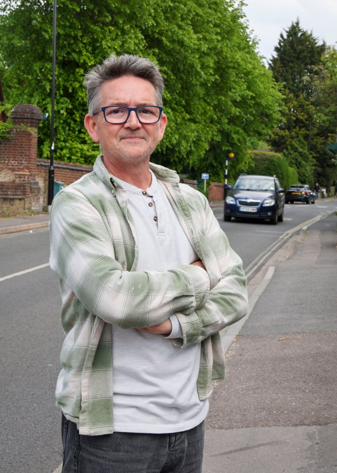 A man stands on a residential street with arms crossed.