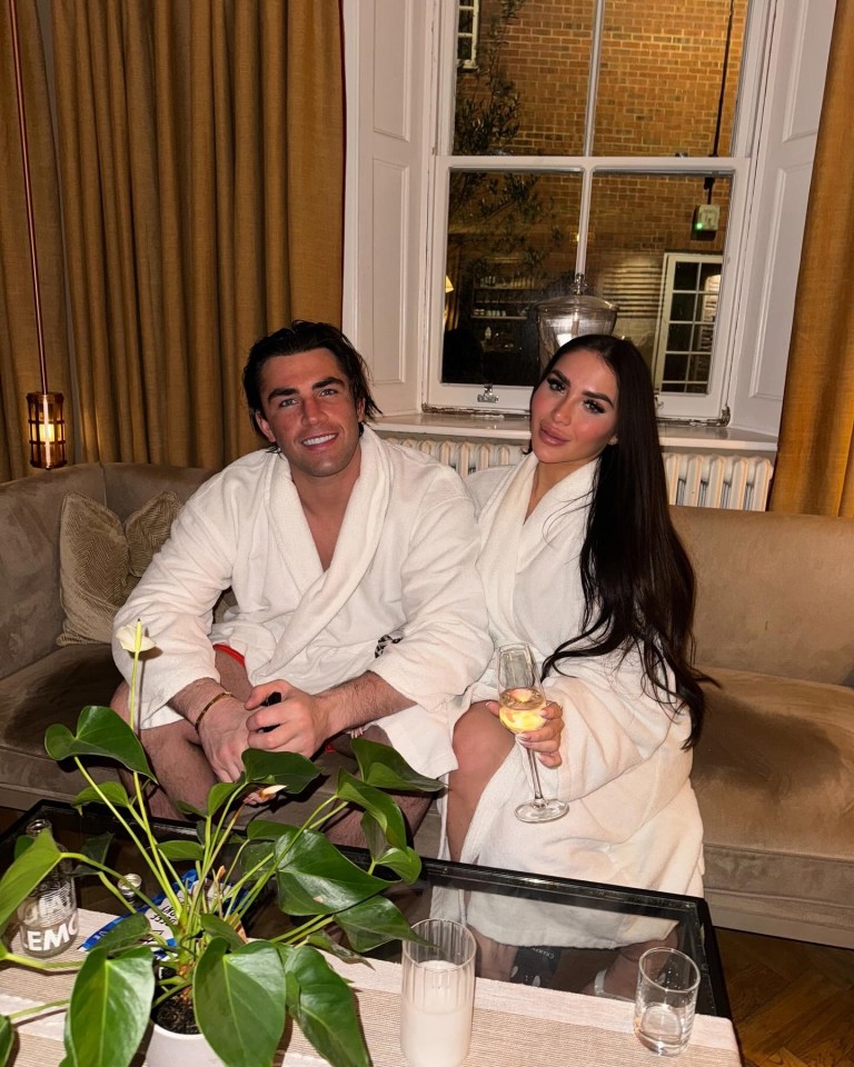 Couple in bathrobes relaxing on a couch with drinks.
