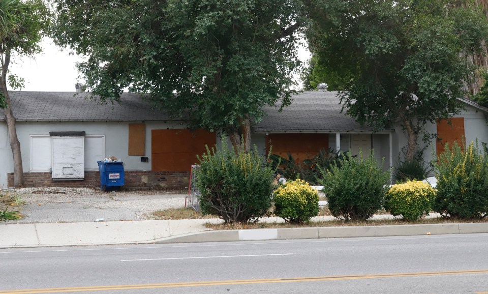 Rundown house with boarded-up windows and a dumpster in front.