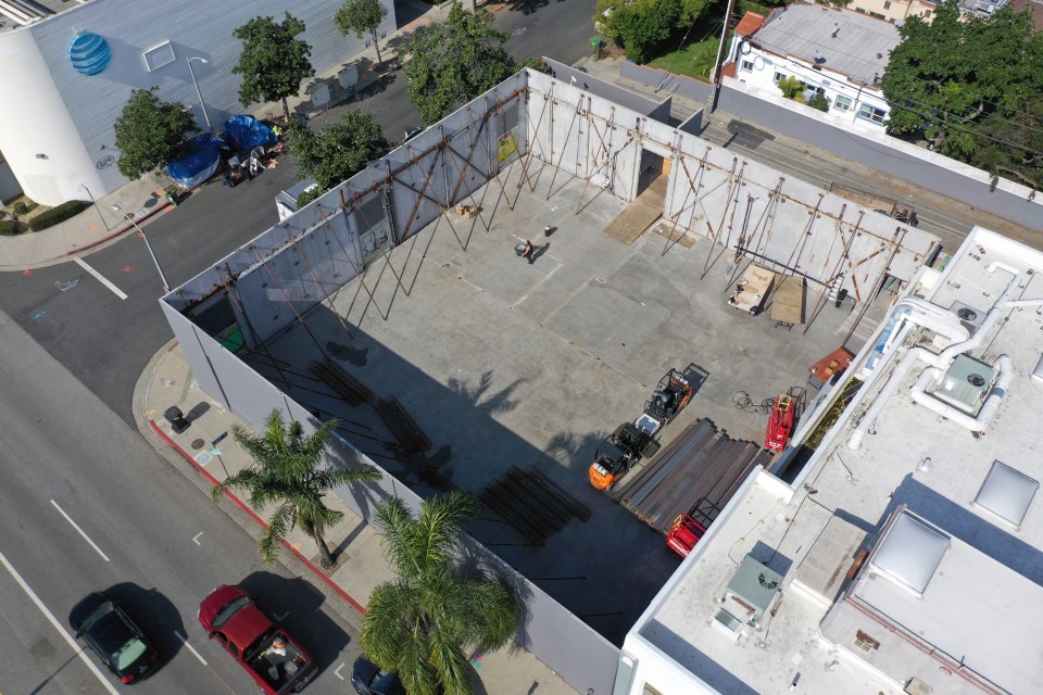 Aerial view of a building under construction with homeless encampments visible across the street.