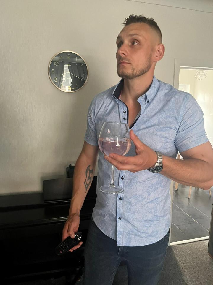 Man holding a glass of wine and a remote control.