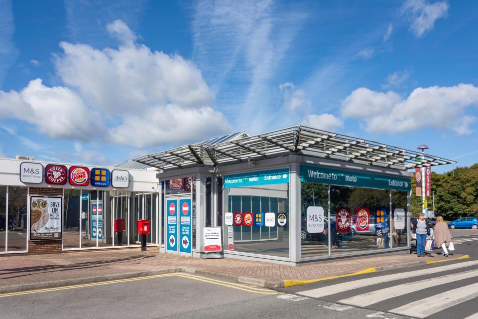 Entrance to Moto Leigh Delamere motorway services with M&S, Costa Coffee, Burger King, and Greggs.
