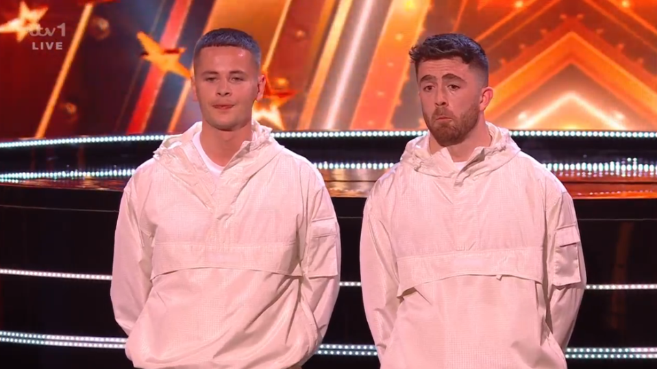 Two men in cream jackets on a TV talent show stage.
